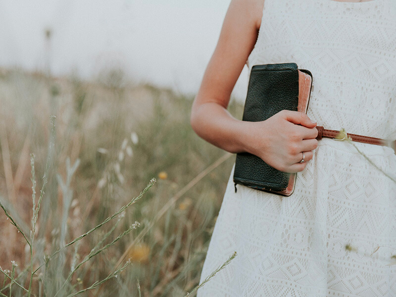 A woman clutching a Bible in a field of wildflowers
